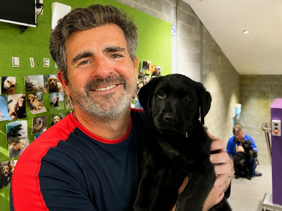 A pro4labs founder smiling and holding a young black Labrador puppy.
